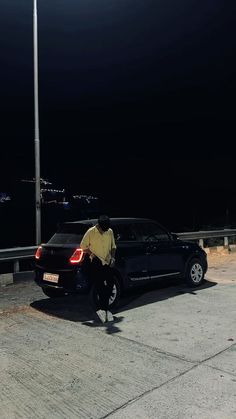 a man standing next to a parked car on the side of a road at night