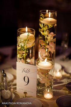 two tall vases filled with flowers and candles on top of a dining room table