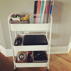 a white cart with books and other items on it next to a wooden floor in a room