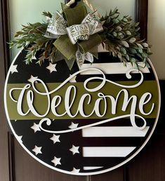 a welcome sign hanging on a door with greenery in the center and an american flag design