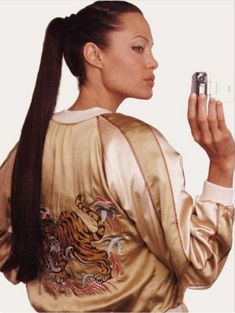 a woman holding a cell phone in her right hand and wearing a satin jacket with tiger designs on it