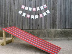 a red and gray striped bench sitting in front of a wooden fence with a happy birthday banner on it