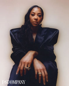 a woman sitting on the floor with her hands folded over her chest and wearing gold rings