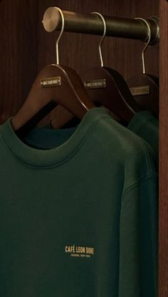 three green shirts hanging on wooden hangers