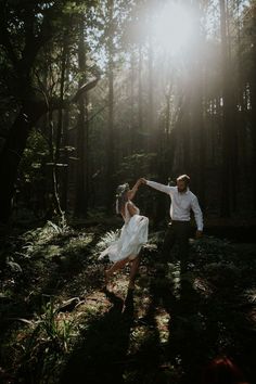 a man and woman dancing in the woods at their wedding day with sun shining through the trees