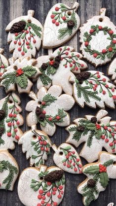 christmas cookies decorated with holly, pine cones and berries are arranged on a wooden surface