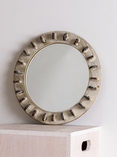 a round mirror sitting on top of a wooden shelf next to a white painted wall