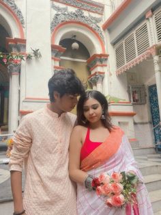 a man and woman standing next to each other in front of a building with flowers