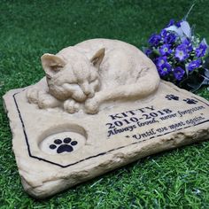 a cat statue laying on top of a pet memorial in the grass next to flowers