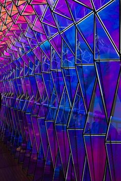 an abstract image of colorful glass covering the building's walls and walkways, with people walking by