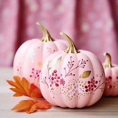 three pink painted pumpkins sitting on top of a table next to an orange leaf