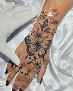 a woman's hand with a butterfly and flowers tattoo on the left wrist, next to white gloves