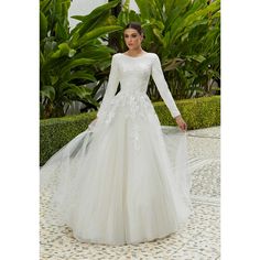 a woman in a white wedding dress standing on a tiled floor with greenery behind her