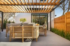 an outdoor patio with wooden furniture and wood slats on the roof, surrounded by greenery