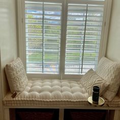 a window seat with two pillows on it in front of a window that has shutters