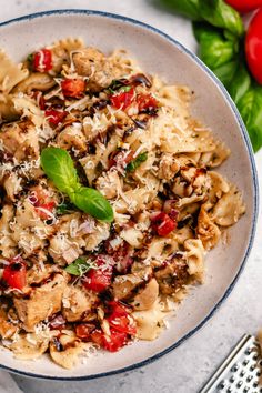 a white bowl filled with pasta and vegetables on top of a table next to tomatoes