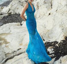 a beautiful woman in a blue dress standing on rocks near the ocean with her hands on her hips