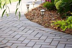 a brick path with two lights on each side and flowers in the backround