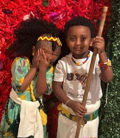 two young children standing next to each other in front of a flower wall with red flowers