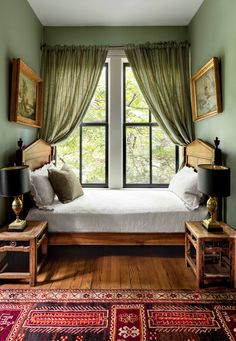 a bed sitting under a window next to two tables with lamps on top of them