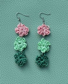 two crocheted flower earrings hanging from hooks on a green leather textured surface