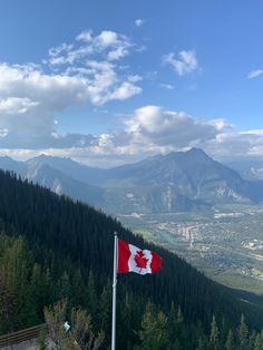 a canadian flag on top of a mountain with trees and mountains in the back ground