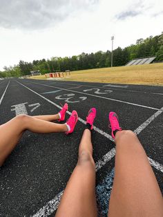 a woman's feet resting on the edge of a running track with pink shoes