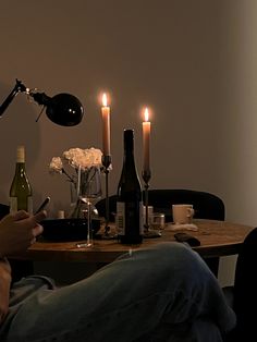 a person sitting at a table with wine bottles and candles on it, looking at their cell phone