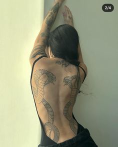 a woman with tattoos on her back is leaning against a wall and touching the wall