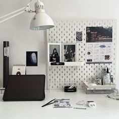 a white desk topped with a laptop computer next to a lamp and pictures on the wall