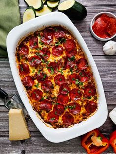 a casserole dish with pepperoni and cheese on it next to sliced zucchini