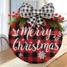 a red and black plaid christmas ornament hanging from a wooden table with holly wreaths