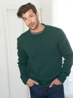 a man standing in front of a white door wearing a green sweater and blue jeans