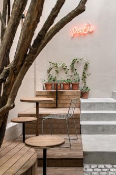 an outdoor seating area with wooden tables and chairs next to potted plants on the wall