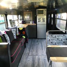 the interior of an rv with wood flooring and black couches, kitchenette and refrigerator