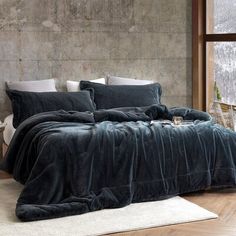 a bedroom with a large bed covered in dark blue blankets and pillows, next to a window