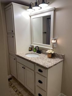 a bathroom with white cabinets and granite counter tops, lights on above the vanity area