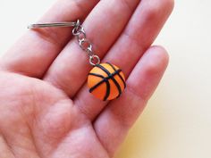 a hand holding a small orange and black basketball keychain