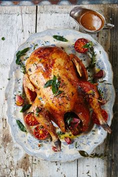 a roasted chicken on a plate with tomatoes and herbs