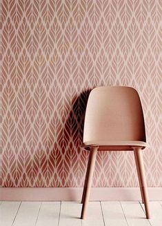 a pink chair sitting in front of a wall with a pattern on the wall behind it