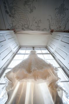 a wedding dress is sitting on the floor in front of an open window with light coming through it