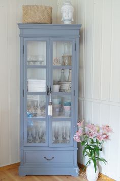 a blue china cabinet with glass doors and flowers in vases on top of it