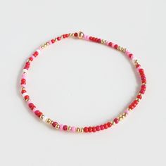 a red and gold beaded bracelet on a white surface with the word love written across it