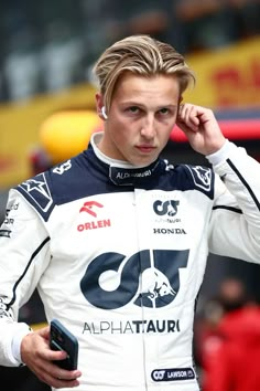 a man in a racing suit talking on a cell phone and holding his hand to his ear