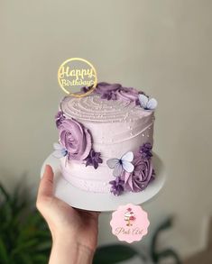 a person holding up a cake with purple flowers on it and a happy birthday sign