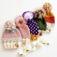 four knitted hats with pom - poms are lined up next to each other