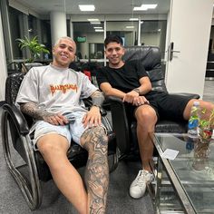 two men sitting in chairs with tattoos on their arms and legs, one is wearing a wheelchair