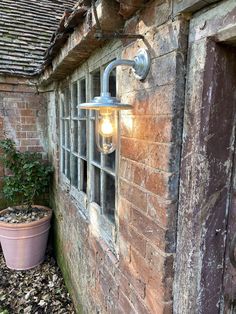 an old brick building with a window and light on the outside wall next to a potted plant