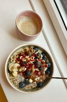 a bowl of cereal with blueberries and bananas next to a cup of coffee