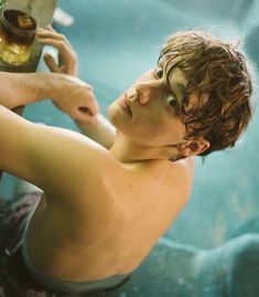 a young man sitting in the water holding a bottle and looking at something off to the side